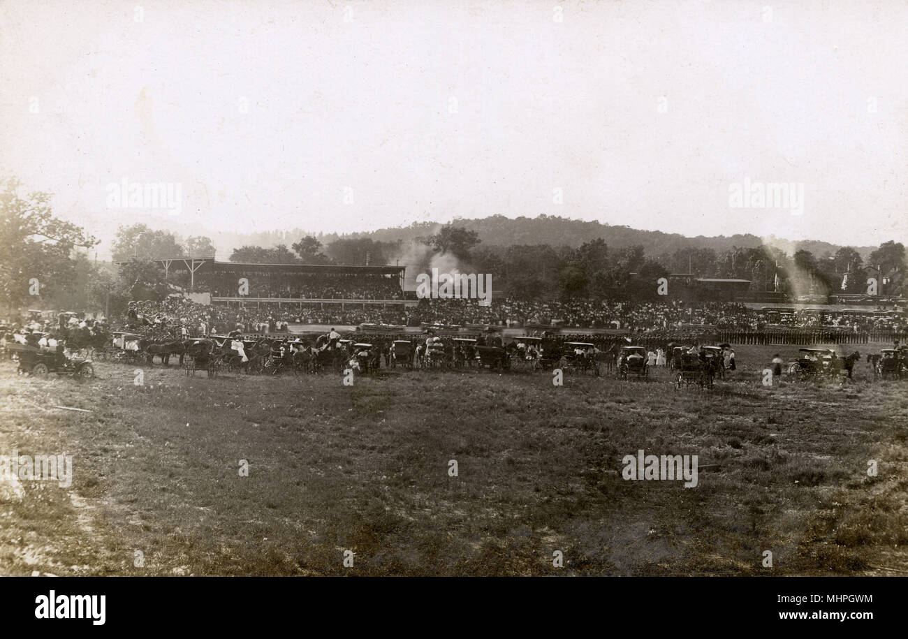 Cancha de deportes en el área de Rock Island, Illinois, EE.UU., con una gran multitud y un desfile militar en curso. En el fondo de la línea de ferrocarril es un vagón etiquetados Rock Island muebles. Fecha: finales de 1910s Foto de stock