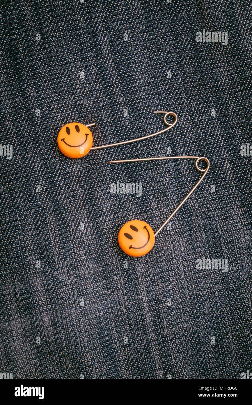 Pasadores de seguridad metálico de cabeza de plástico fijada en jeans de material. Emoticones sonrisa naranja el pasador de seguridad. Lindo y divertido coloridos iconos gestuales. Foto de stock