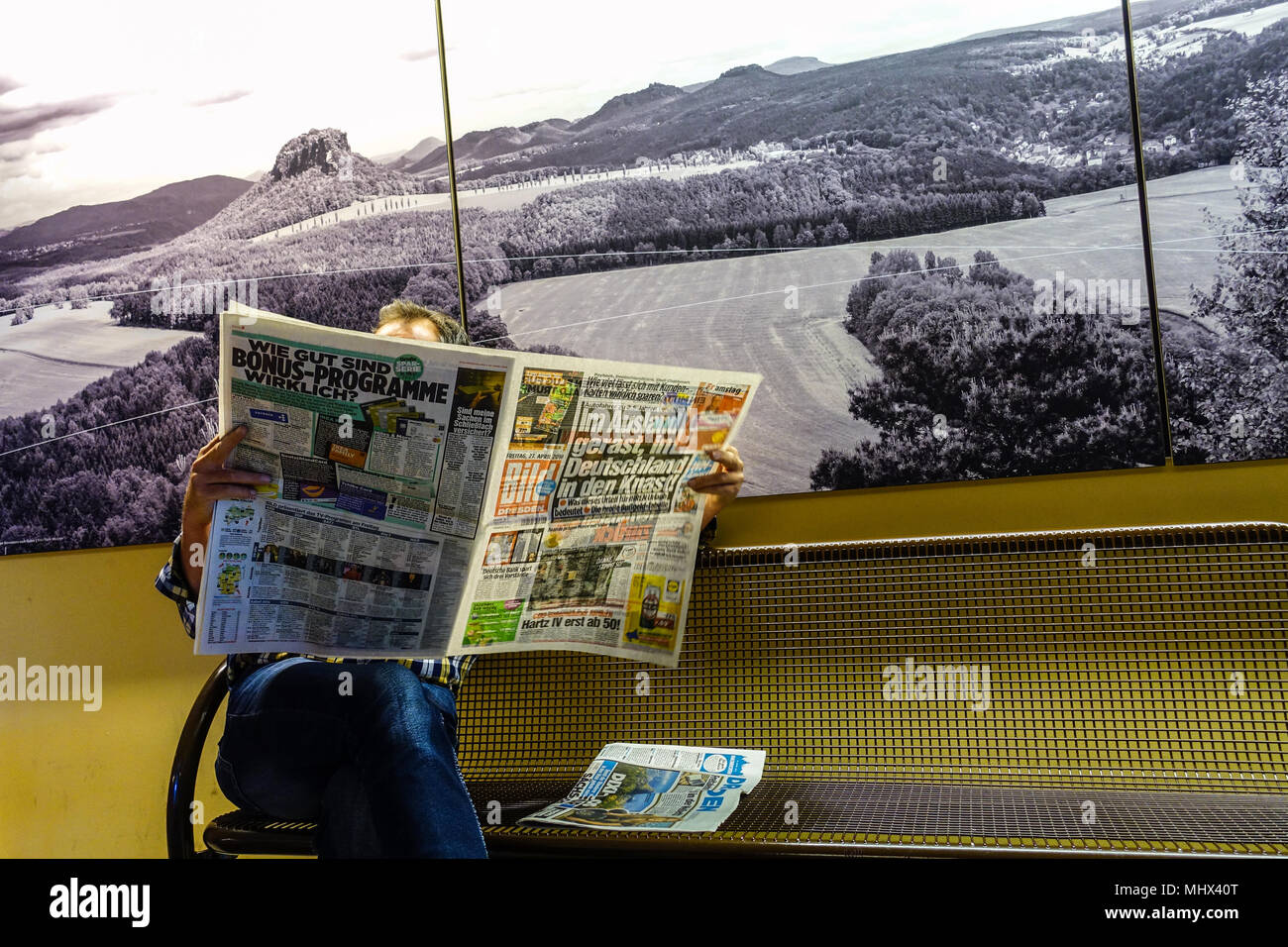 El lector lee el periódico alemán Bild en la estación de ferrocarril, Bad Schandau, foto de fondo el paisaje de la suiza sajona, alemán Foto de stock