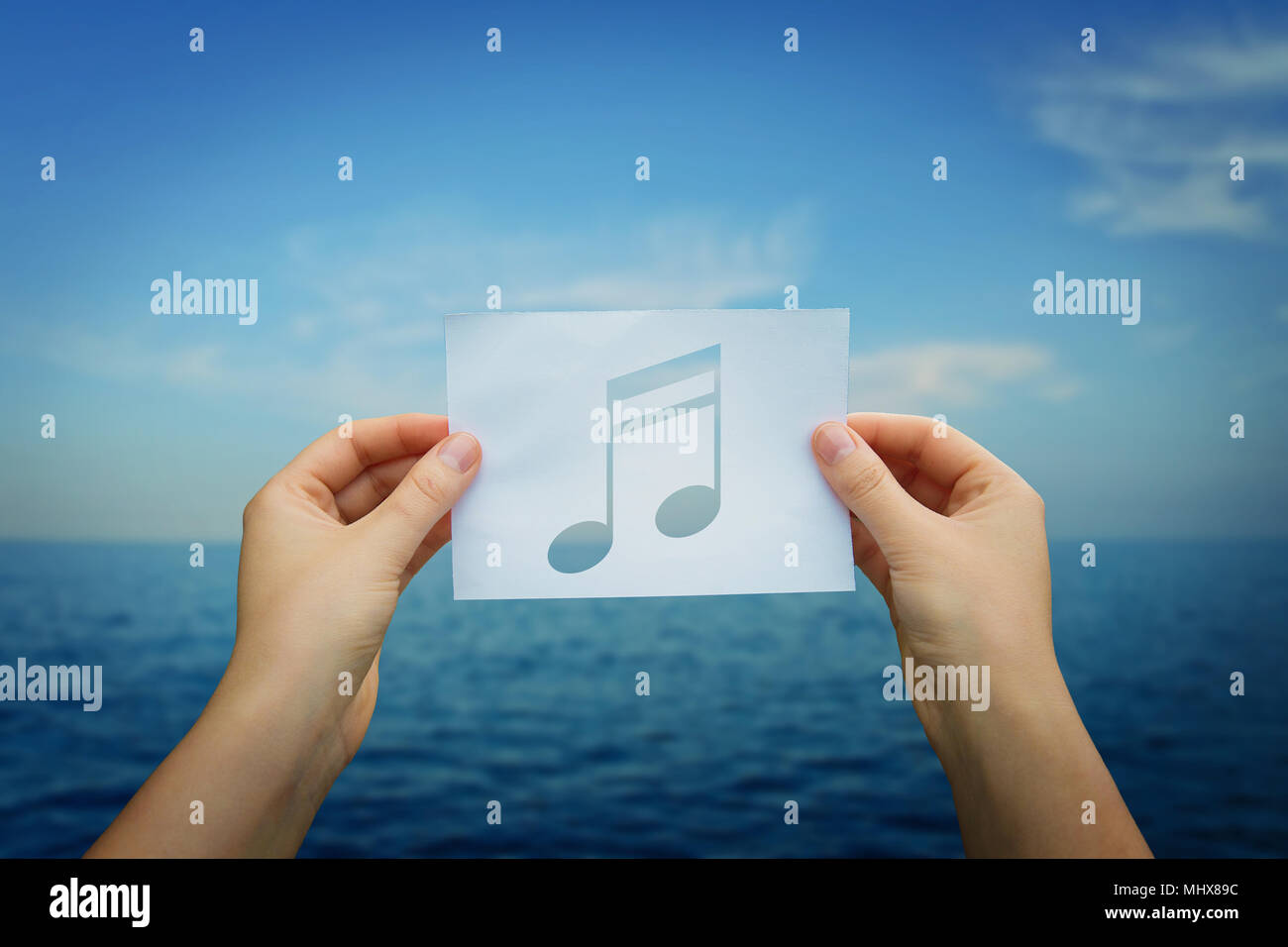 Mujer manos sosteniendo una hoja de papel con música nota dentro, sobre el  horizonte azul del mar de fondo. Escuchando al ritmo de las olas del océano  Fotografía de stock - Alamy