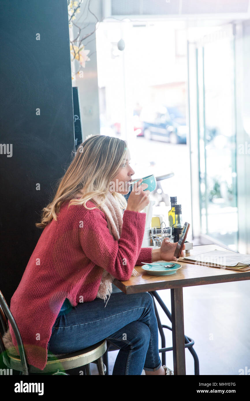 Mujer sentada en el café, beber café, sujetando el smartphone Foto de stock