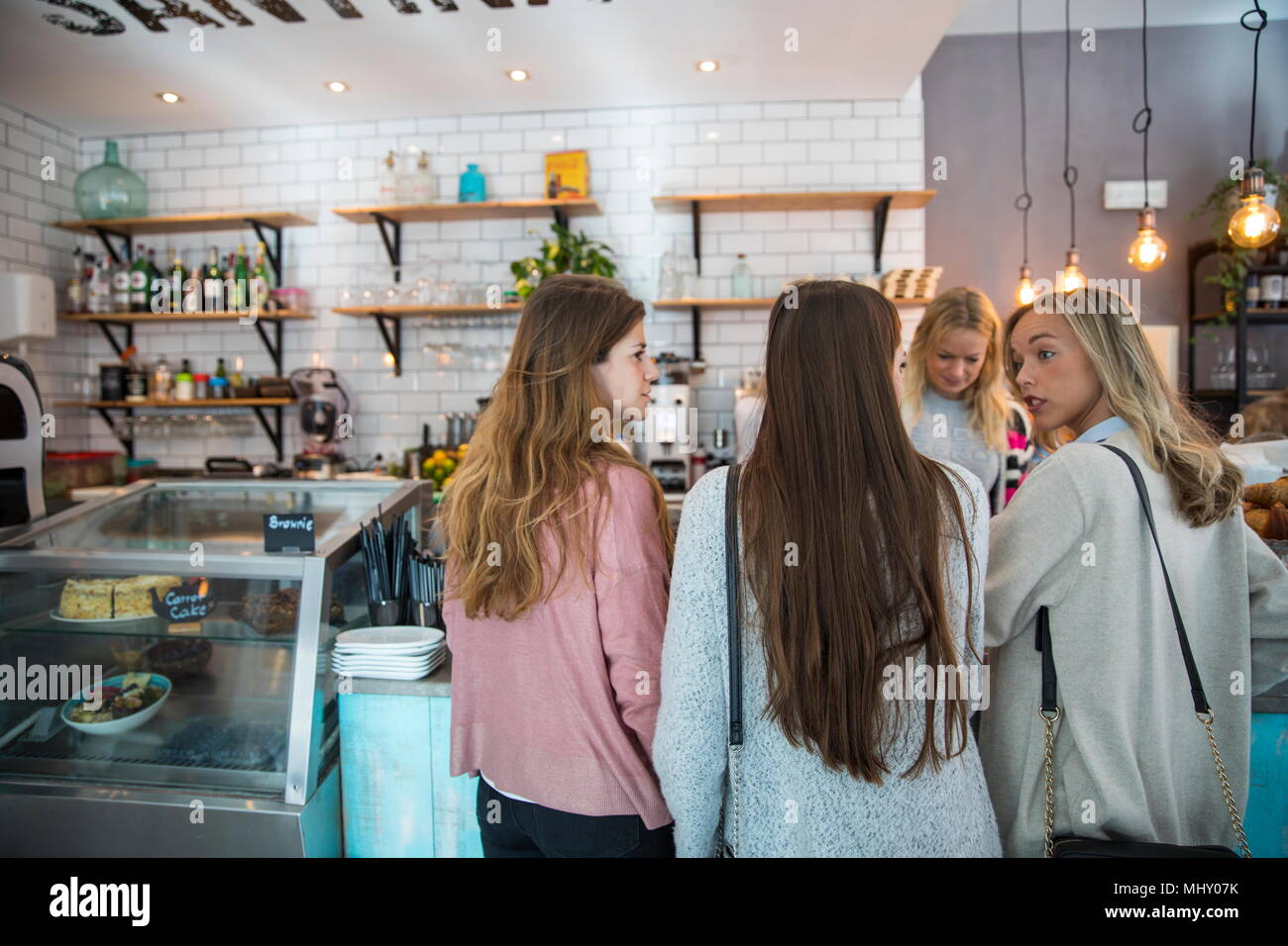 Tres amigas, de pie en el mostrador en el cafe, vista trasera Foto de stock