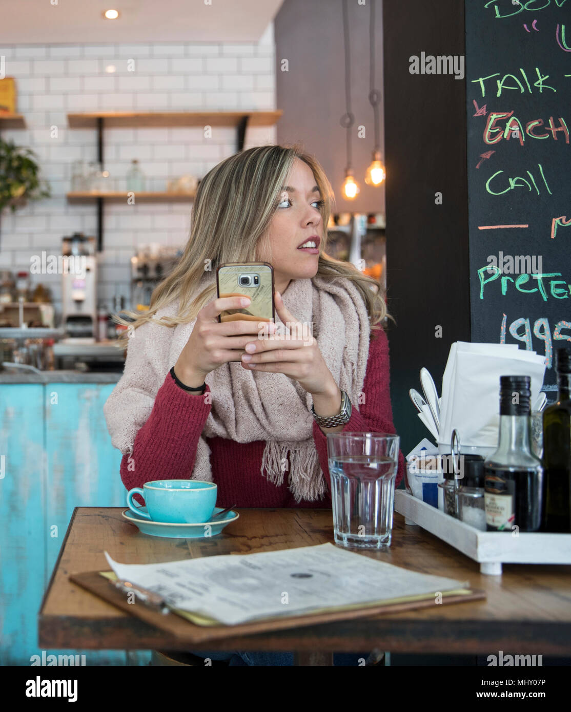 Mujer sentada en el café, sujetando el smartphone, mirando lejos Foto de stock