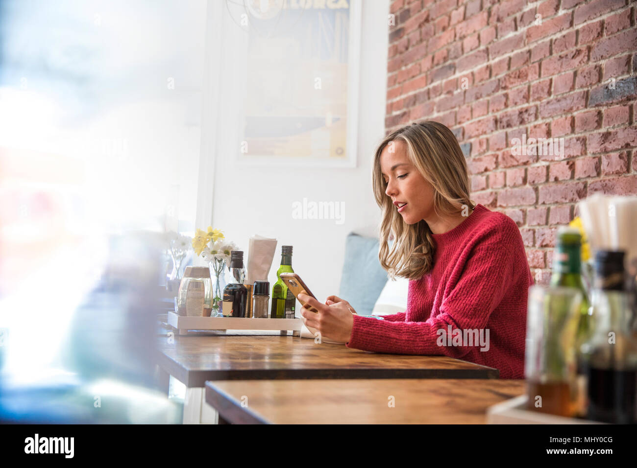 Mujer sentada en la cafetería, mirando el smartphone Foto de stock