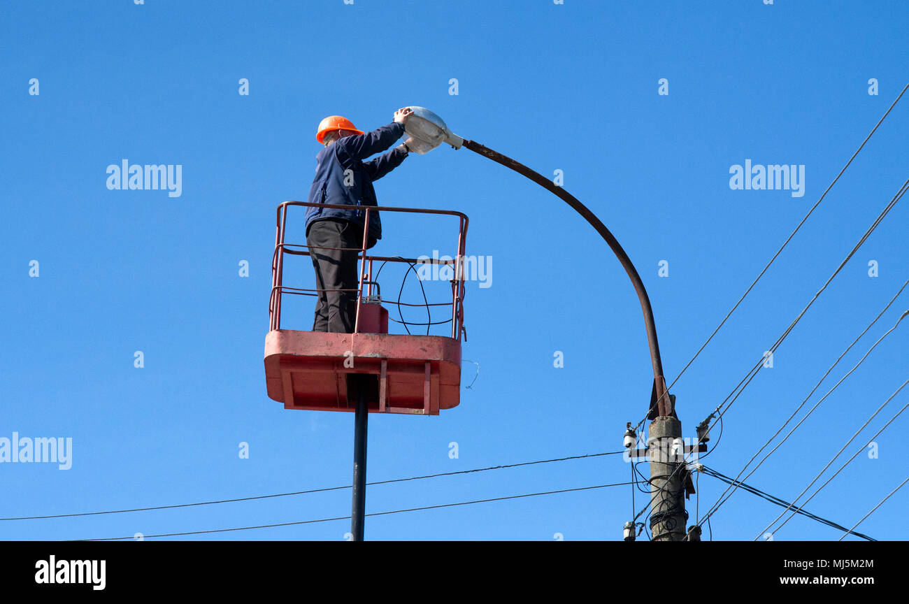 Electricista subir instalando nuevos trabajos sobre la energía eléctrica lámpara de la calle polo de hormigón en blue sky Foto de stock