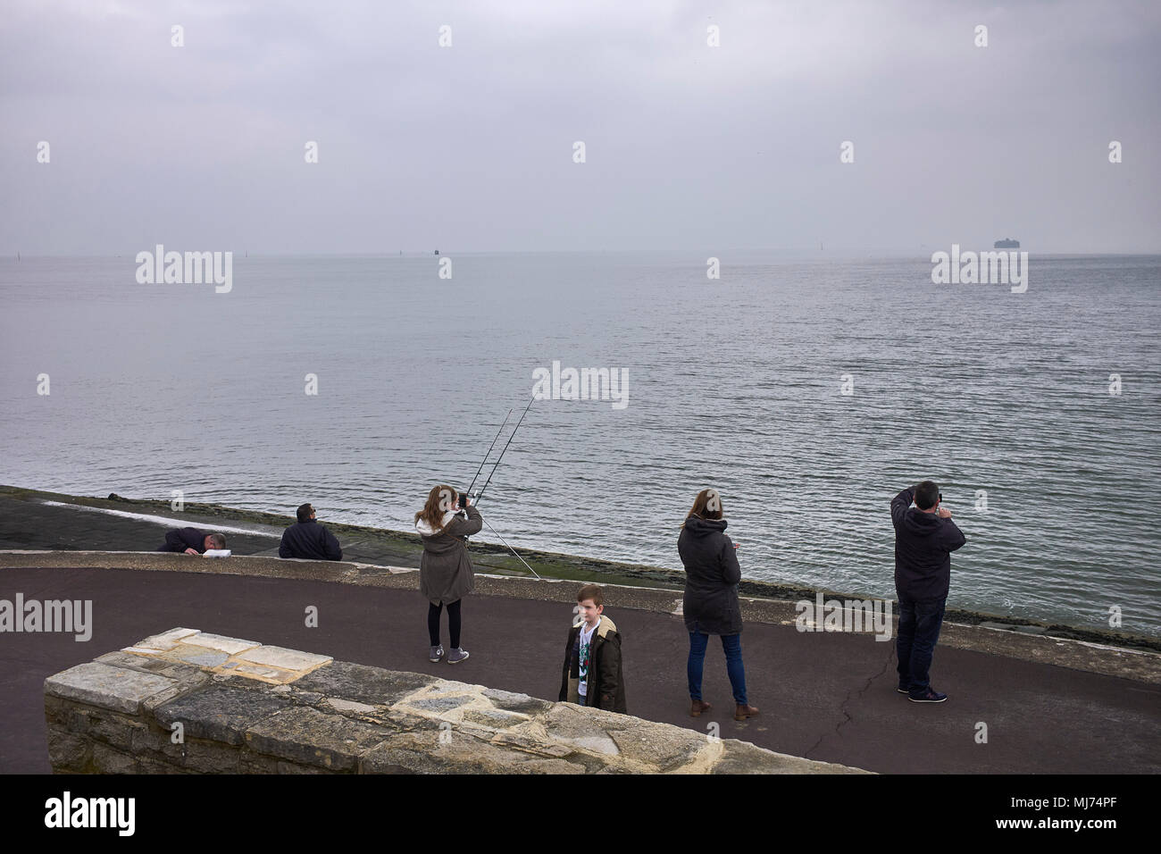 Una familia parada para tomar fotos de teléfono hacia el mar mientras un niño mira hacia la cámara en Southsea, Hampshire Foto de stock