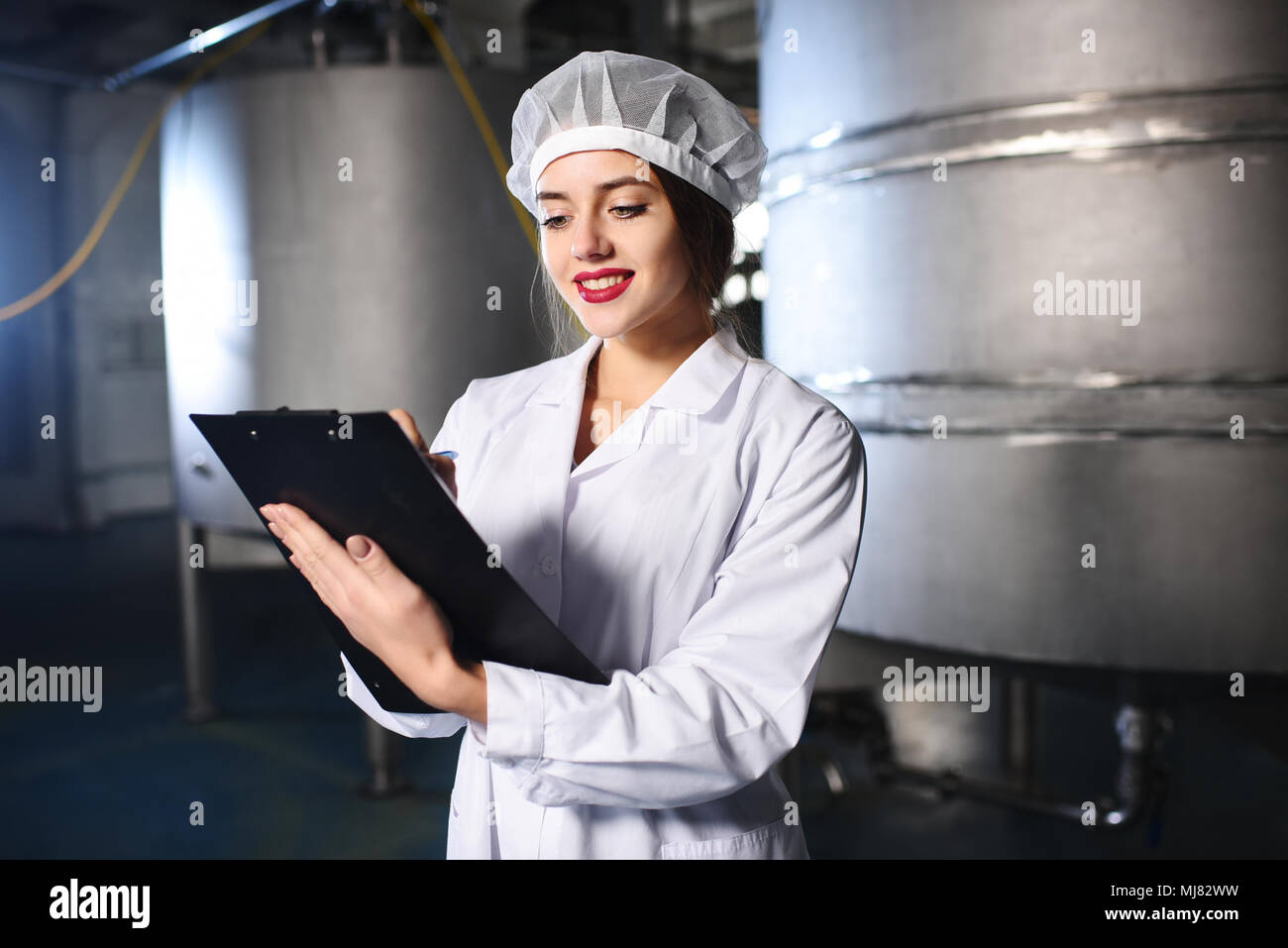 Chica científico o trabajador en blanco uniforme hace que las notas en papel, con el telón de fondo de la moderna fábrica de equipos. Foto de stock