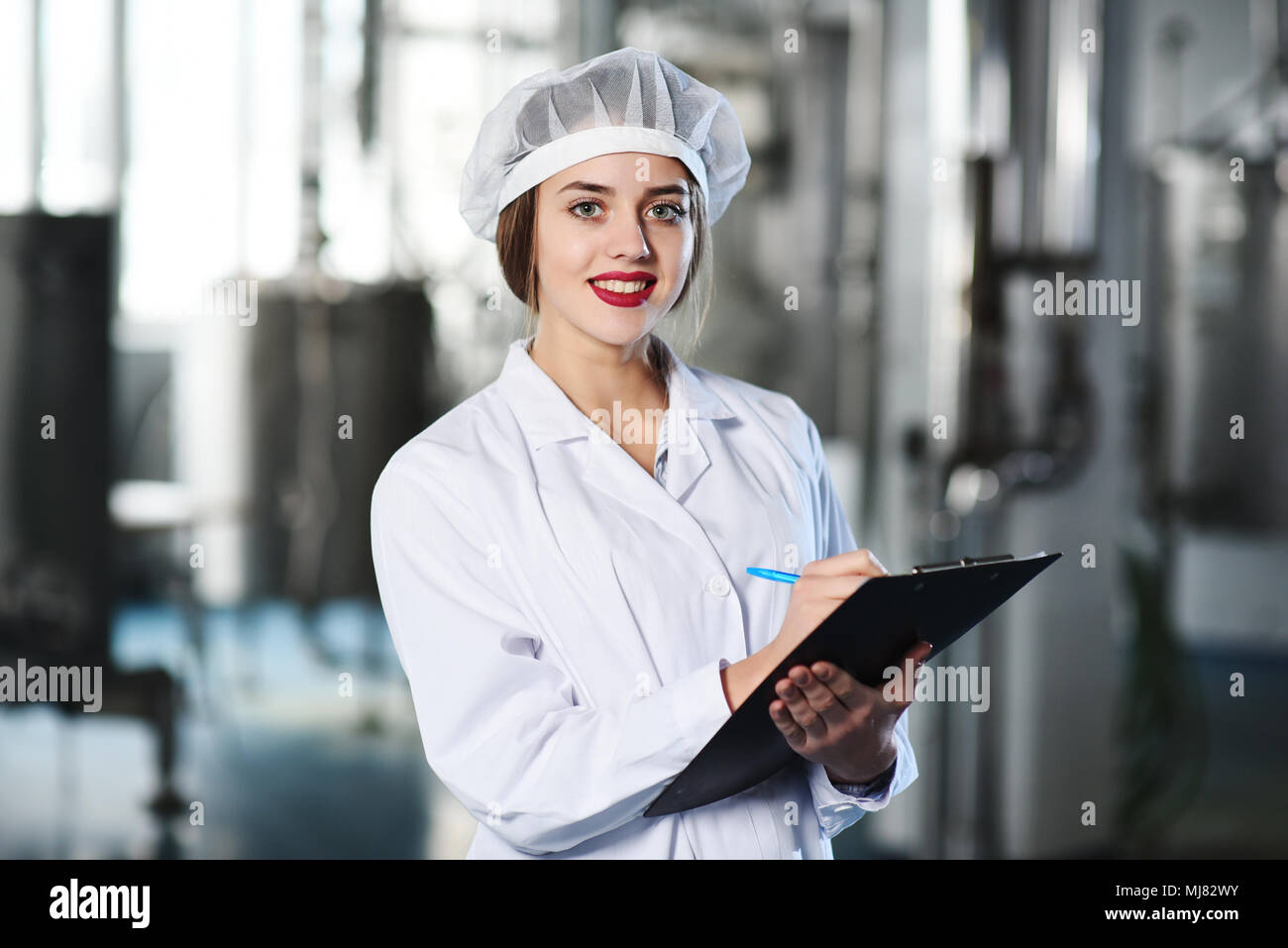 Chica científico o trabajador en blanco uniforme hace que las notas en papel, con el telón de fondo de la moderna fábrica de equipos. Foto de stock