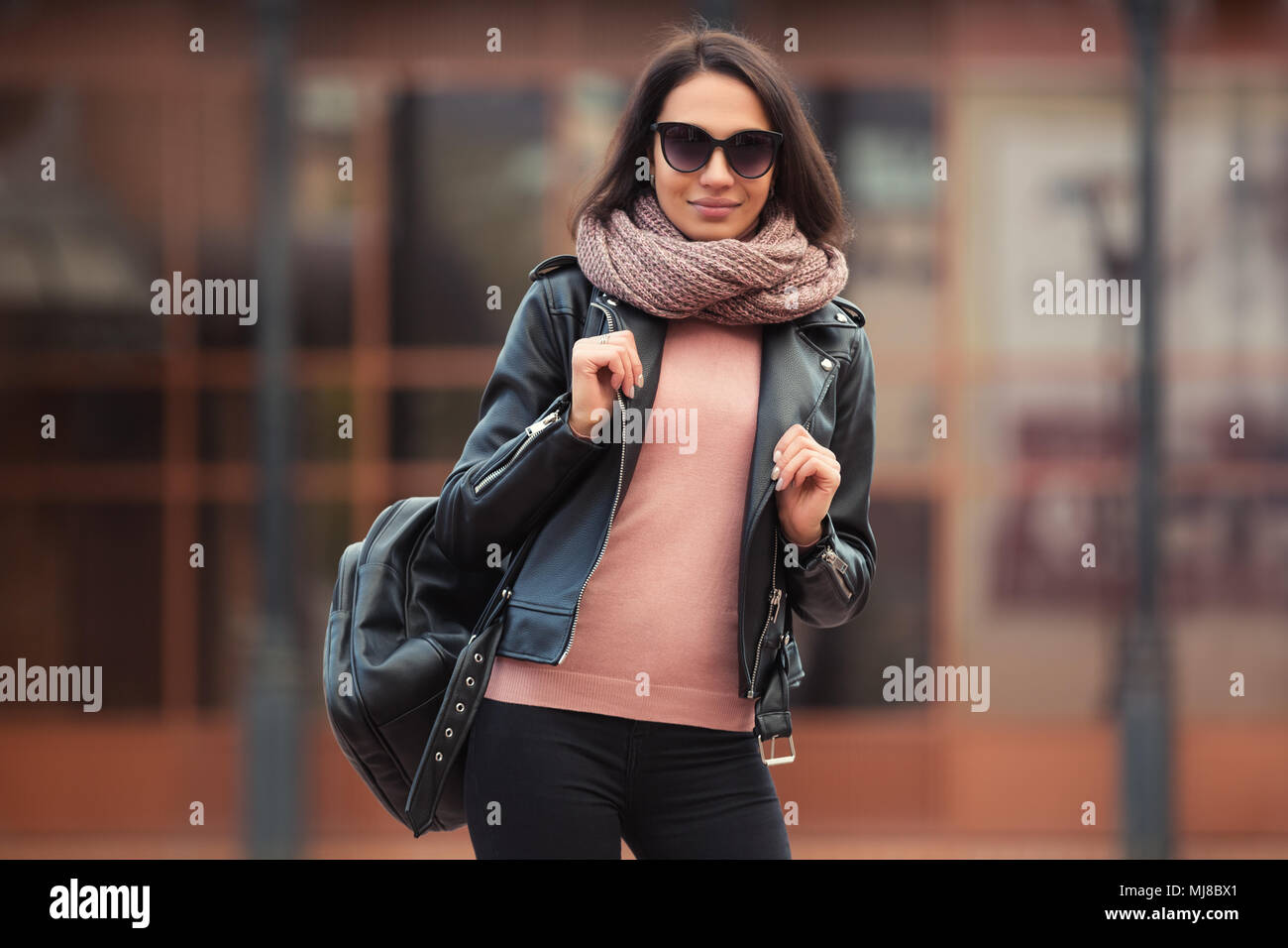 Moda joven mujer con mochila caminando por las calles de la ciudad Elegante modelo femenino en la chaqueta de cuero negro en el exterior Foto de stock
