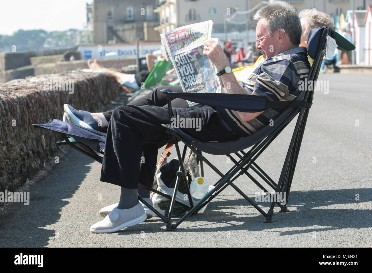 Un hombre las capturas con las noticias en el sol en Paignton paseo marítimo. Foto de stock
