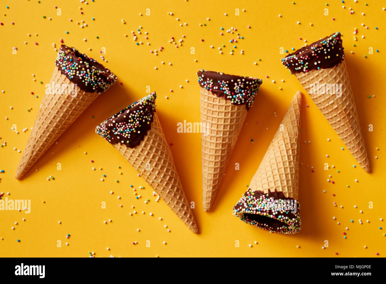 Cono de helado con coloridos rocía sobre fondo amarillo. Foto de stock