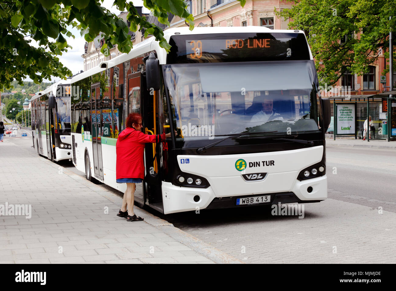 Harnosand, Suecia - Julio 5, 2017: Una anciana con ropa roja camina a bordo del autobús de la ciudad blanca en el tráfico en línea 39 Min Tur en la parada de autobús Foto de stock