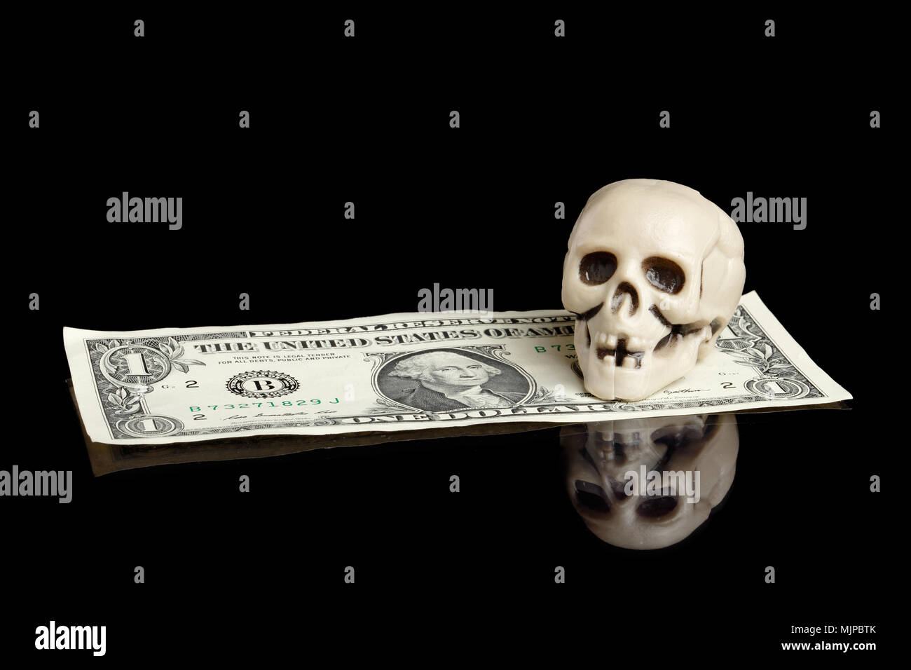 Un cráneo de plástico pequeño en un billete de dólar aislados en negro. Foto de stock