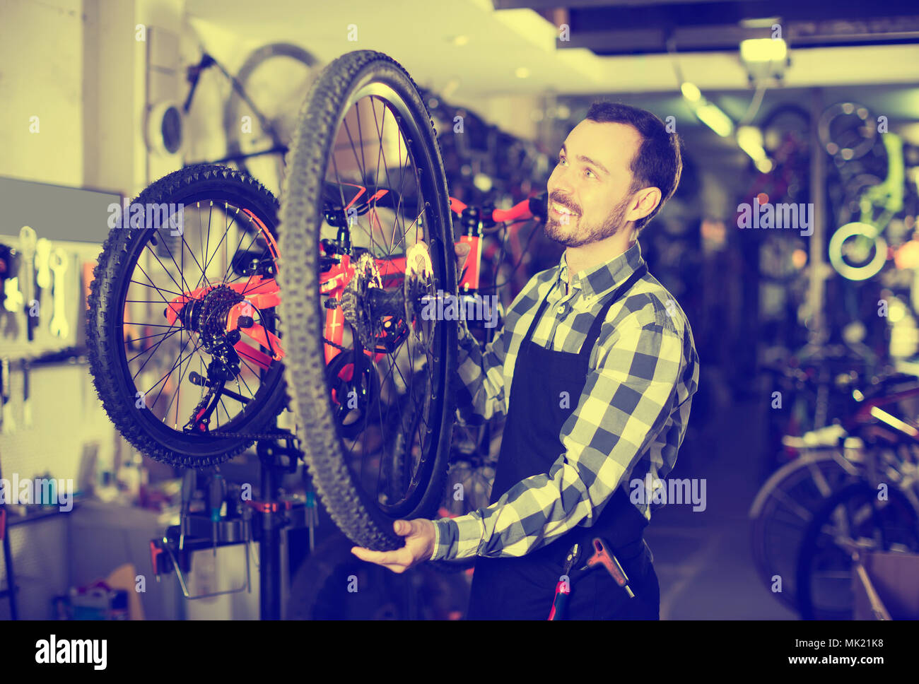 Hombre sonriente maestro establece una rueda de bicicleta en su taller Foto de stock