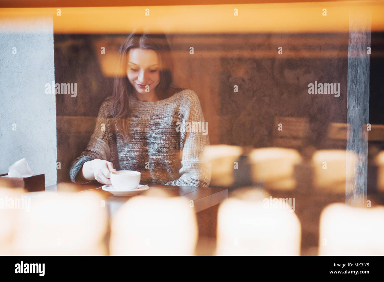 Mujer sonriente en el café a través de teléfono móvil y los mensajes de texto en las redes sociales, sentados solos Foto de stock