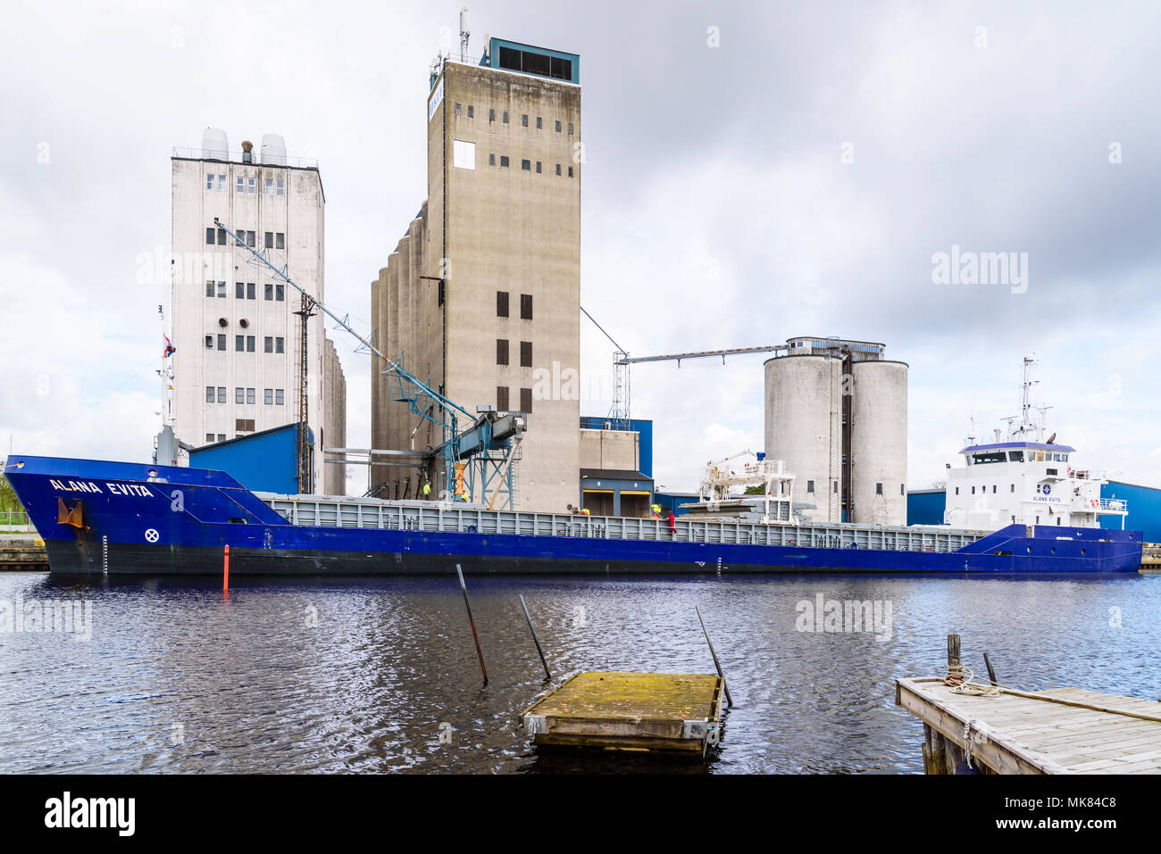Ahus, Suecia - Abril 26, 2018: Viaje documental de la vida cotidiana y el medio ambiente. Los trabajadores cargando el grano en un buque de carga azul en el puerto en un cl Foto de stock