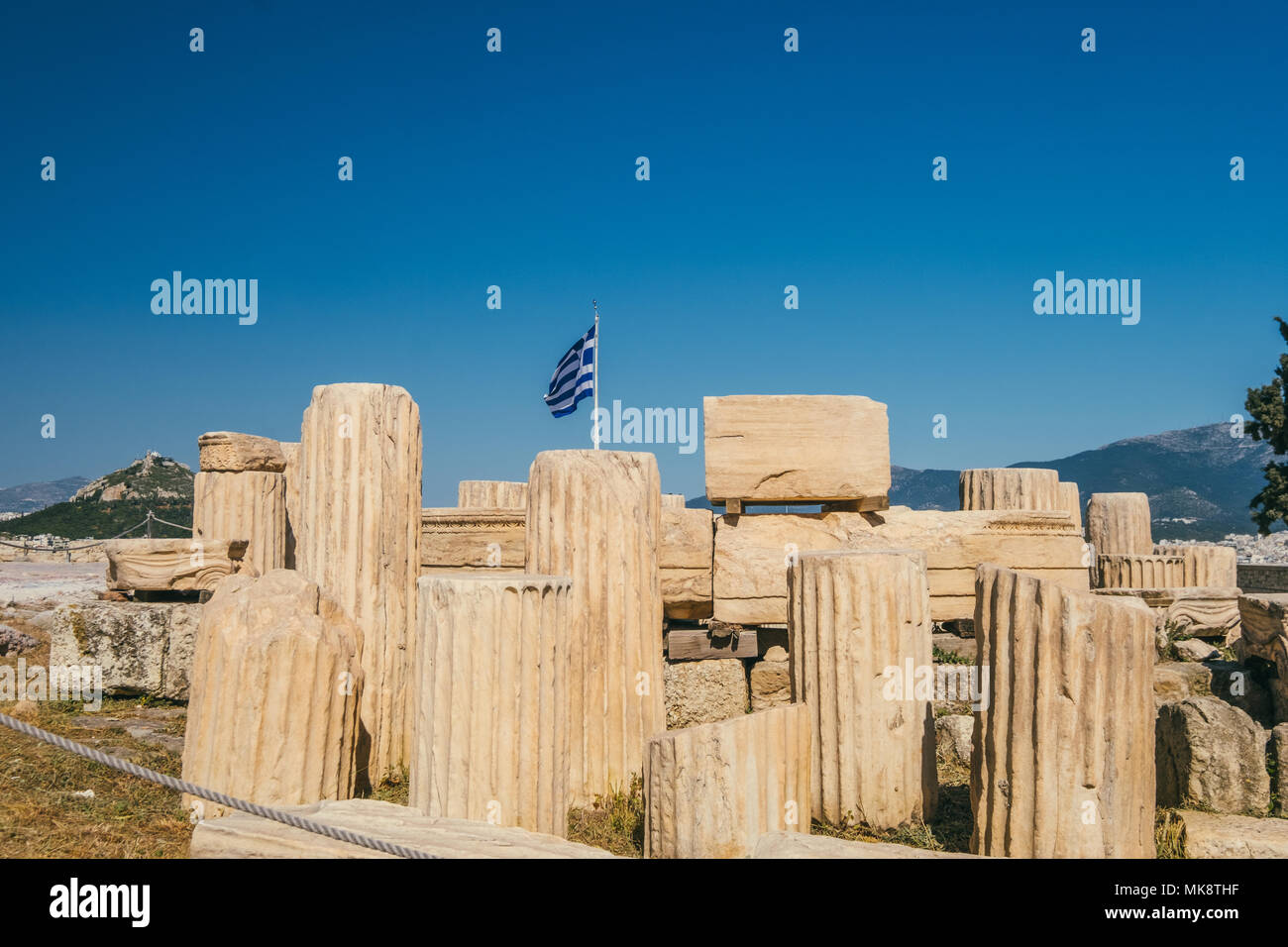 Bandera griega en la Acrópolis, con antiguas columnas griegas en primer plano Foto de stock