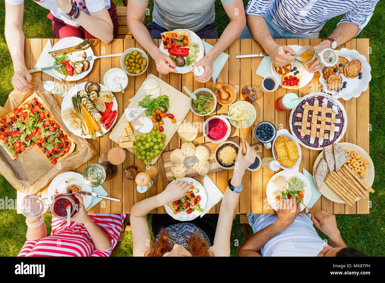 Amigos comiendo alimentos saludables como vegan pizza y fruta al aire libre en el parque en una tabla rústica Foto de stock
