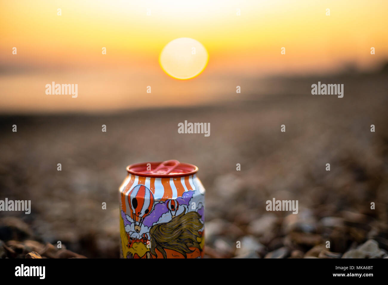 Una colorida lata de cerveza artesanal en una playa con una puesta de sol, fuera de foco en el fondo Foto de stock