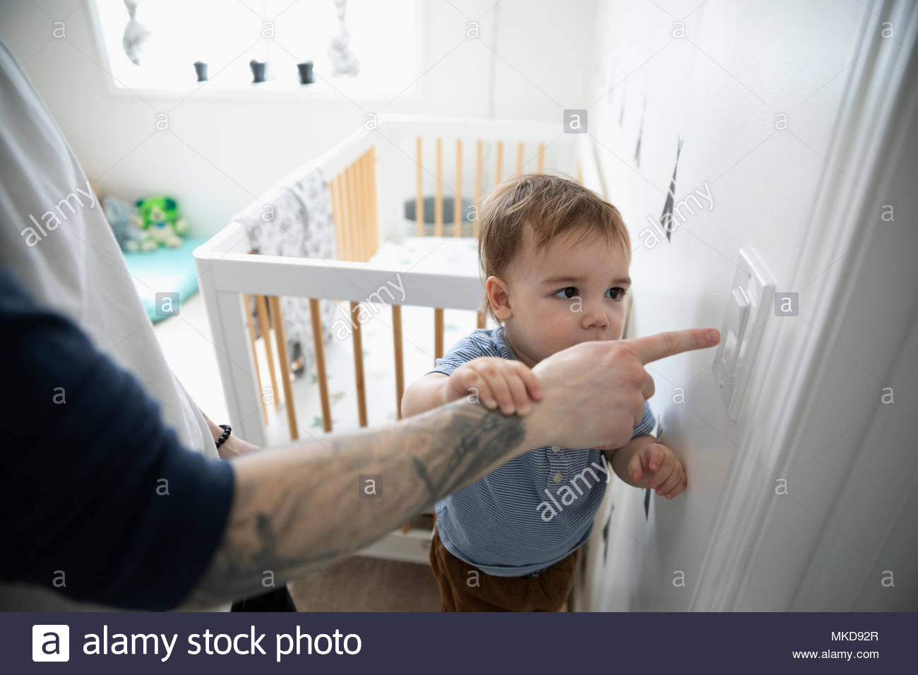 Hijo curioso viendo padre empujando el interruptor de luces en la guardería Foto de stock