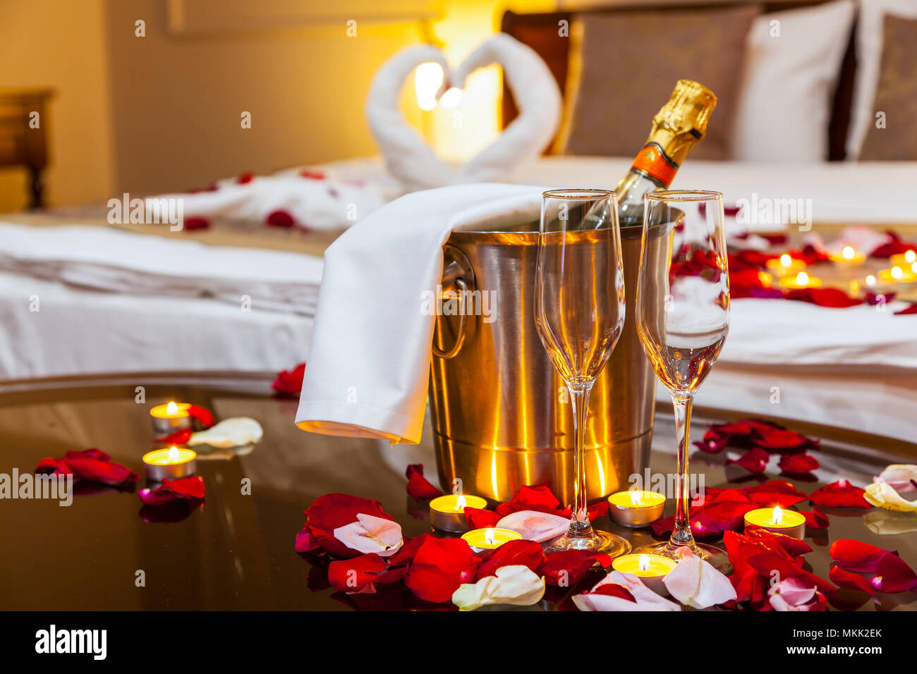 Habitación de hotel para una luna de miel: una mesa con un plato de fruta y  velas, en el fondo una cama decorada con cisnes de toallas y pétalos de rosa  Fotografía