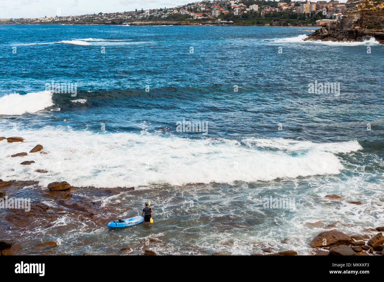 Un hombre sale en la mañana con su bote frente a las olas de la bahía a lo largo de la caminata Coogee a Bondi Beach, Sydney, New South Wales, Australia Foto de stock