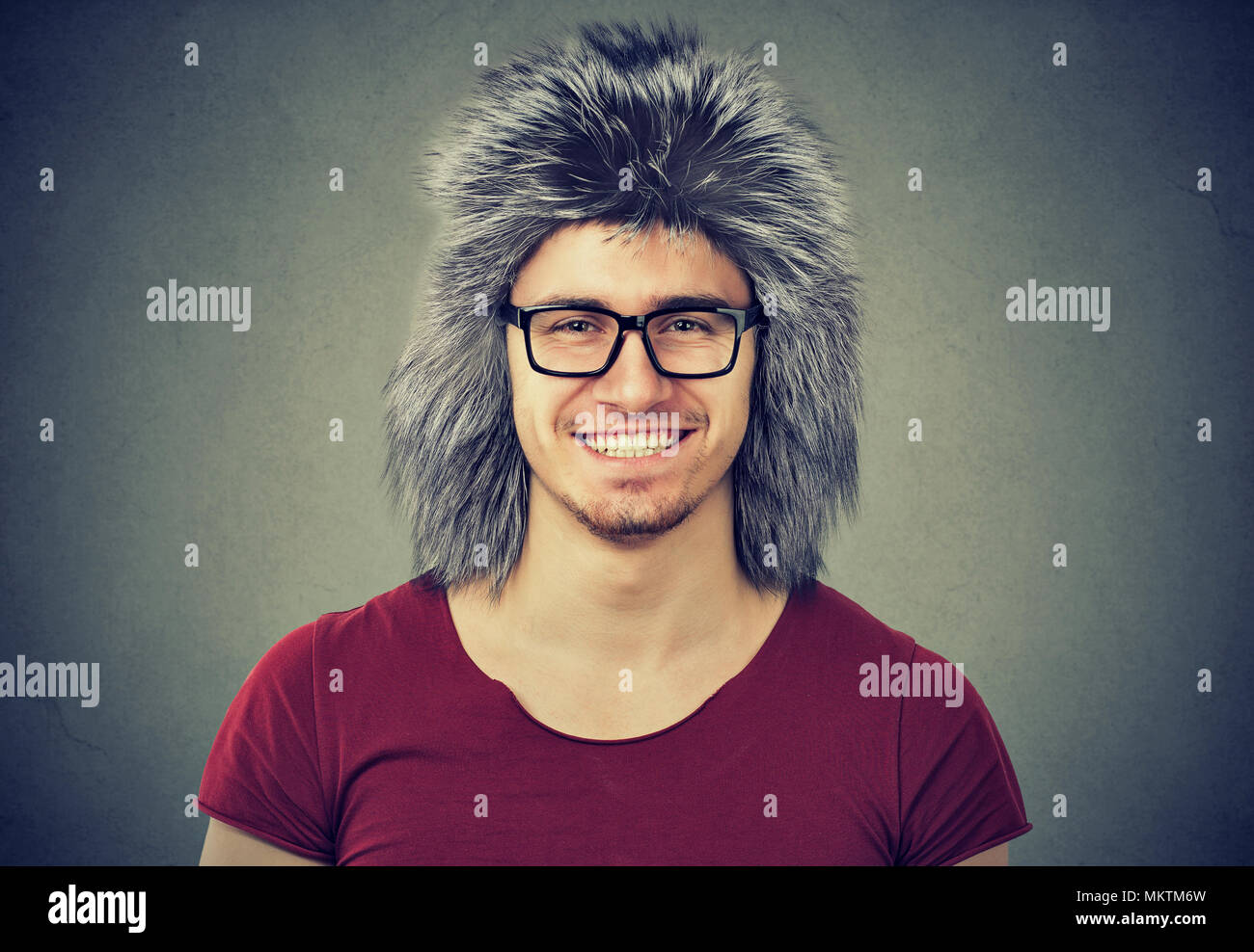 Apuesto hombre sonriente en casual t-shirt y anteojos vistiendo cálido invierno hat sonriendo ante la cámara. Foto de stock