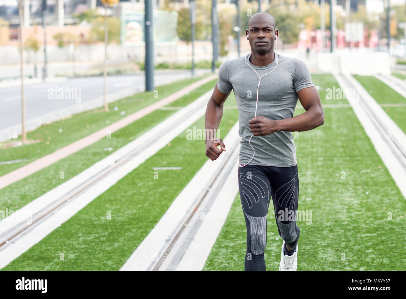 Negro corriendo y escuchando música en el contexto urbano. Hermoso macho haciendo ejercicio al aire libre. Foto de stock