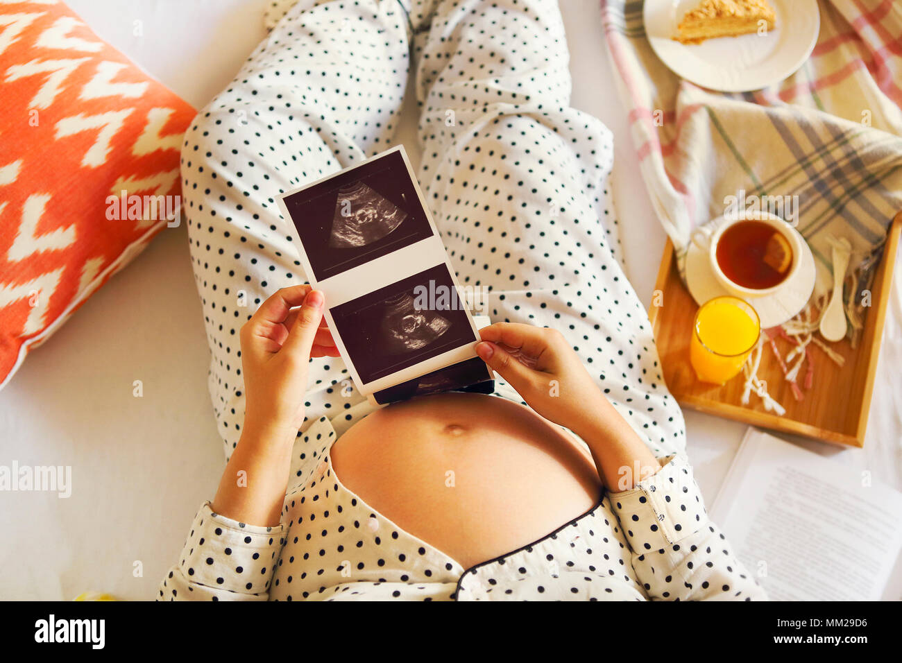 Mujer embarazada vistiendo pijama con libreta, té, pasteles para relajarse en casa. Vista superior Foto de stock