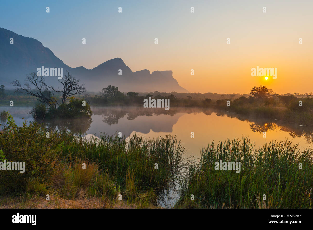 Amanecer con el pico de la montaña Hanglip reflejando en un pantano del lago en el interior de la reserva de caza safari Entabeni, provincia de Limpopo, Sudáfrica. Foto de stock