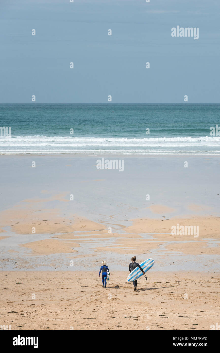 Un adulto y un niño cargando sus tablas de surf caminando en una playa. Foto de stock