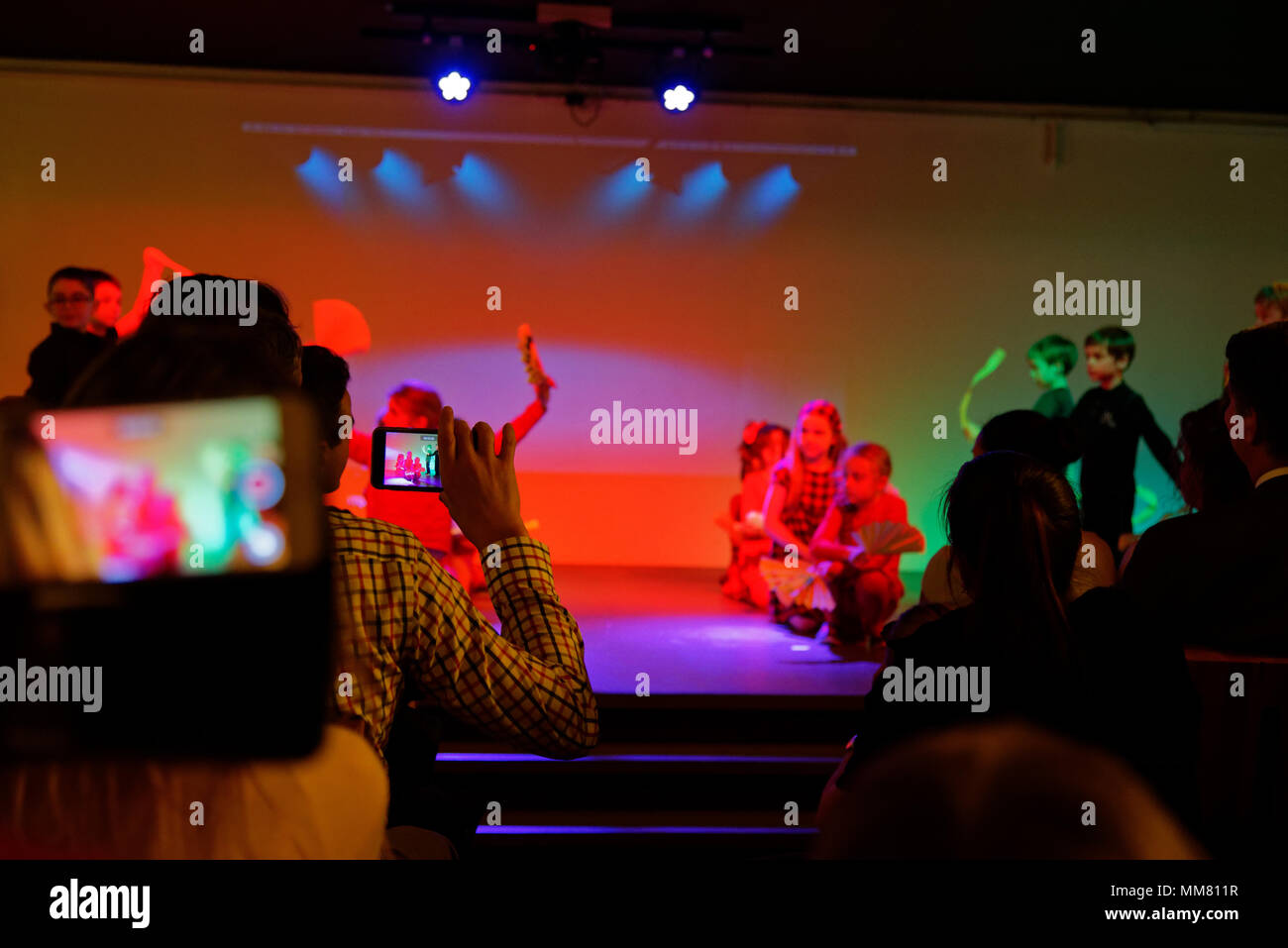 Un hombre filmando un concierto escolar con un iphone Foto de stock