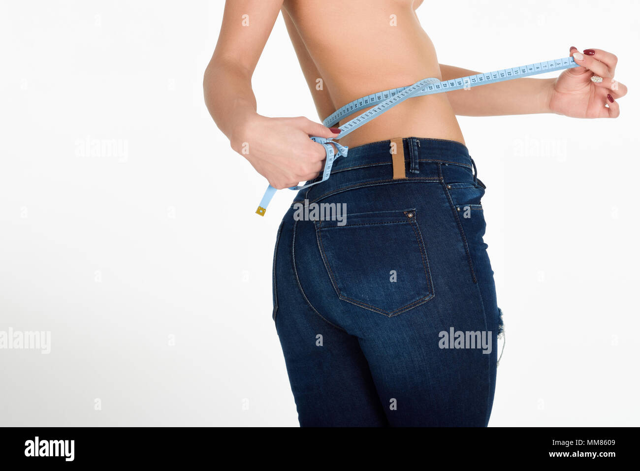 Mujer joven midiendo la cintura con una cinta. Sanos y chica con pantalones vaqueros azules sobre fondo blanco. Foto de stock