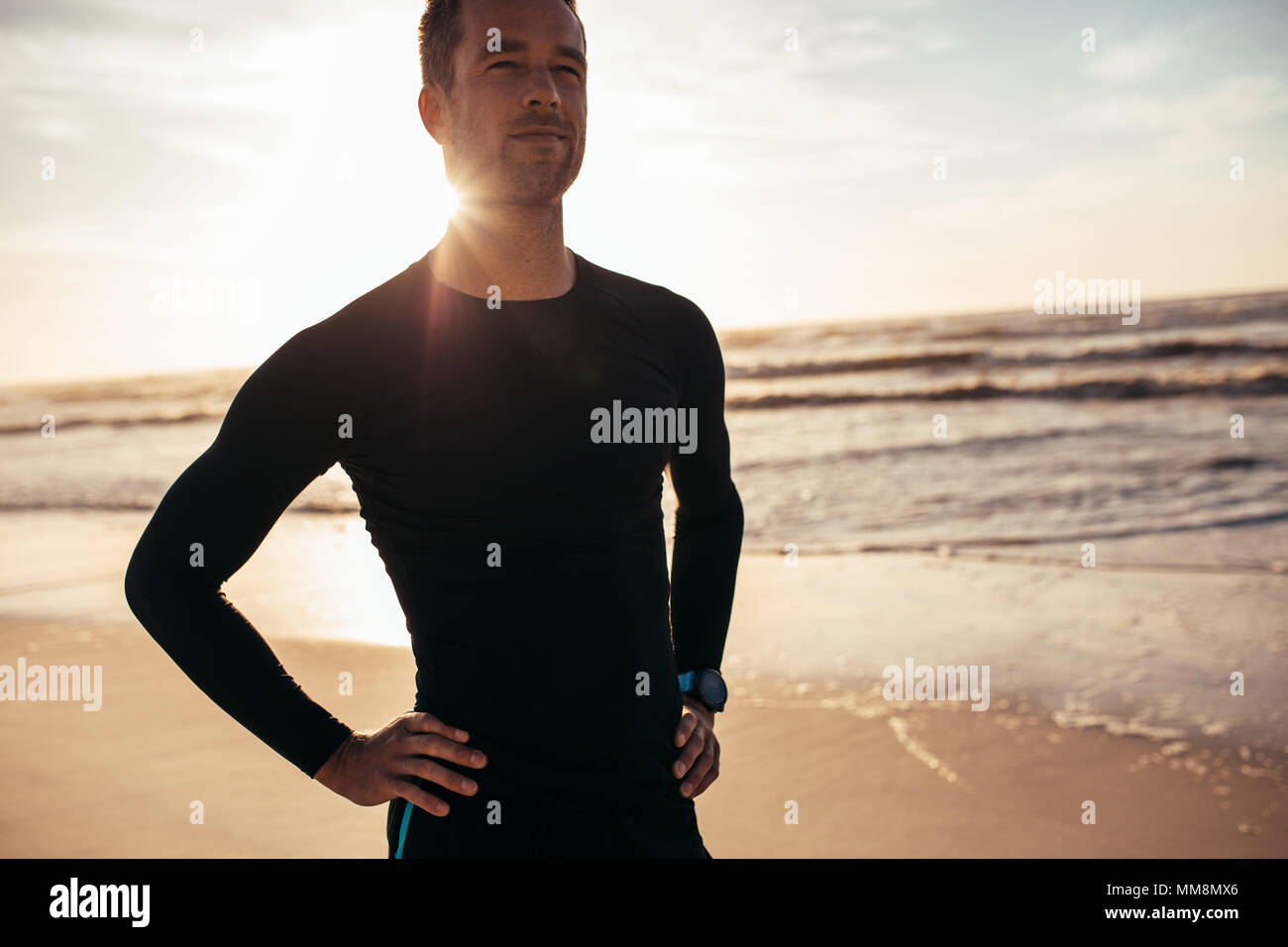 Retrato de seguros atleta masculino de pie en la playa. Hombre en ropa deportiva a lo largo de la orilla del mar en la mañana. Foto de stock