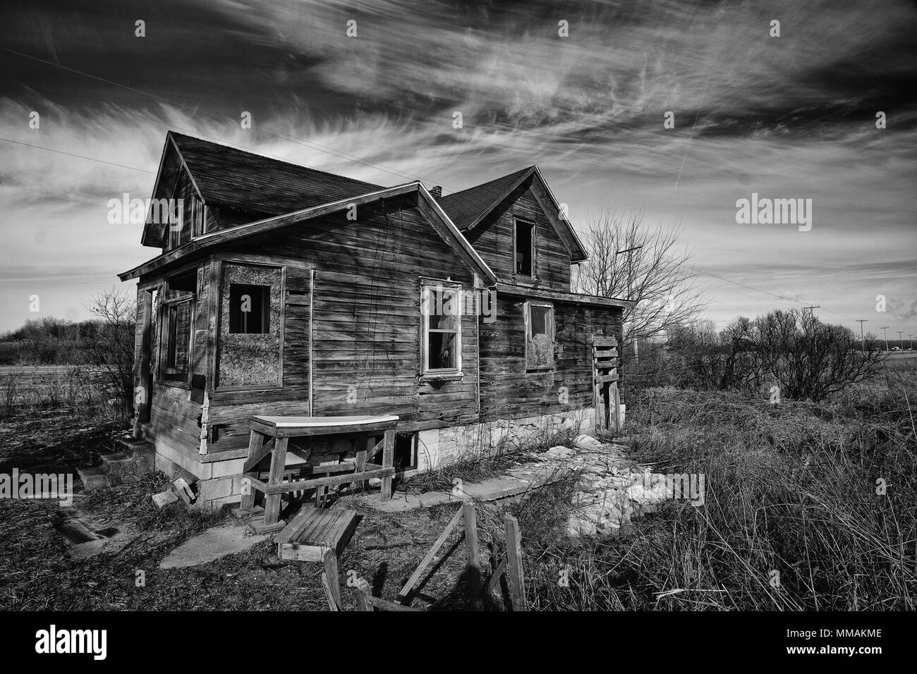 Fotografía en blanco y negro de una antigua casa de granja abandonada de miedo que se está deteriorando con el tiempo y el abandono. Foto de stock