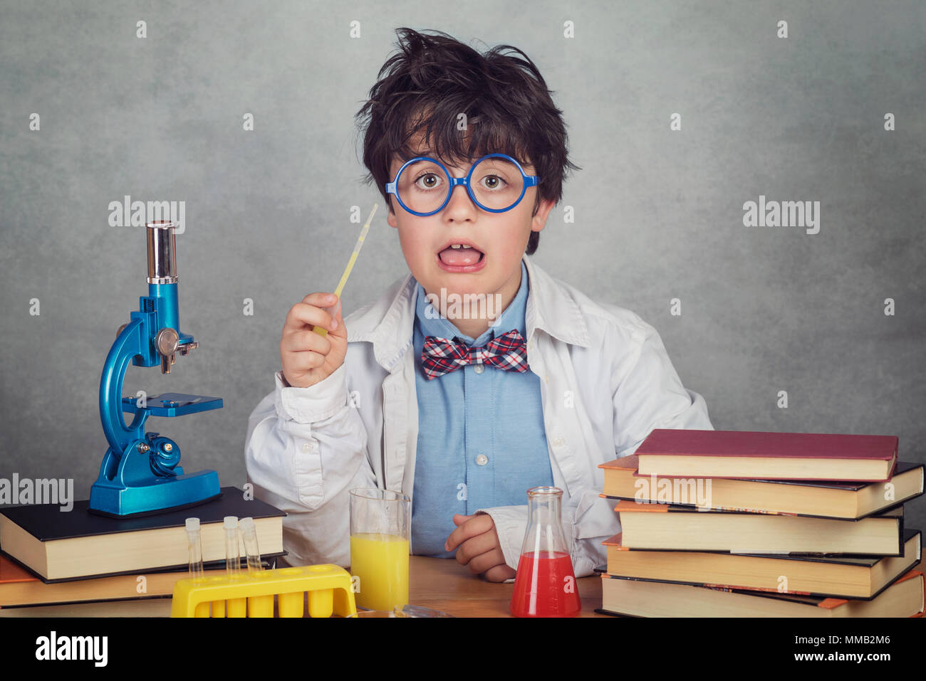 Chico es realizar experimentos científicos en un laboratorio sobre fondo gris Foto de stock