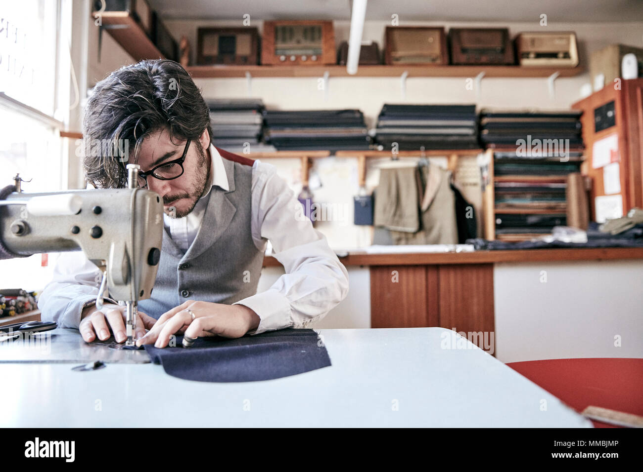 Hombre coser una prenda utilizando una máquina de coser industriales, en un taller de sastrería familiar. Foto de stock