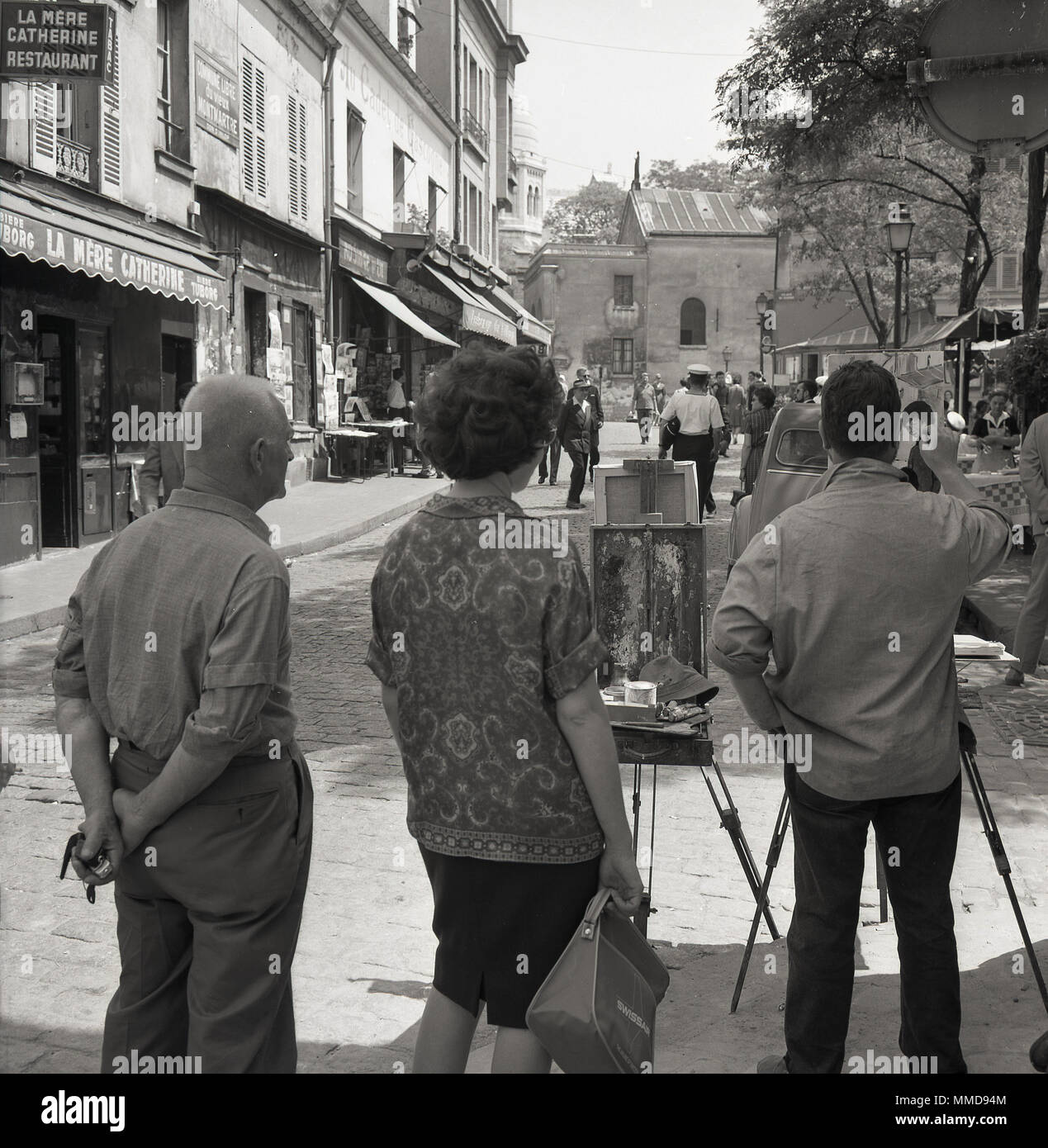 1950, Montmartre, Paris, Francia, un par ver un artista callejero masculino trabajando en su caballete en la Place du Tertre, famosa por sus pintores, y portraitists historia artística. Foto de stock