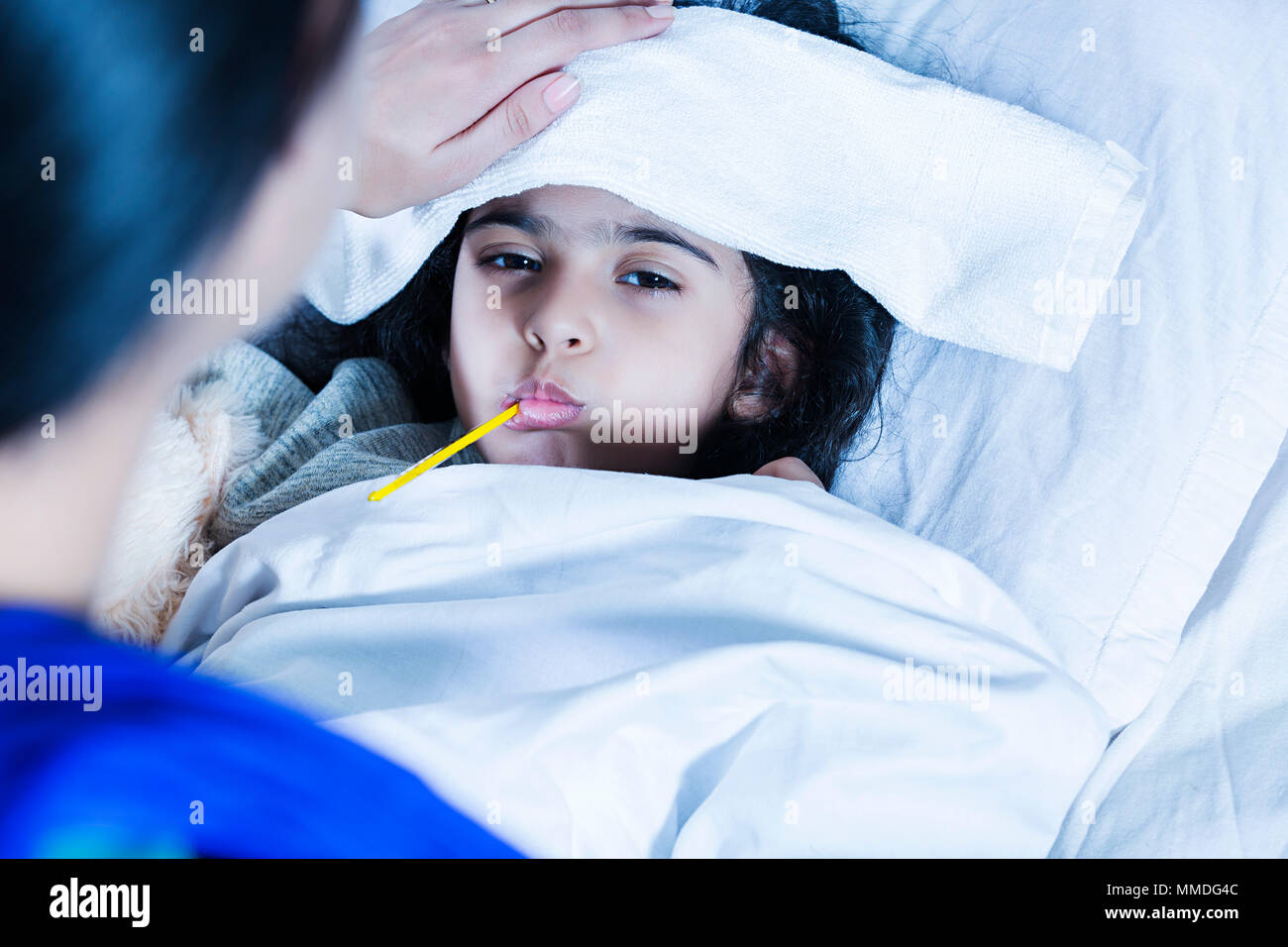 Chica control de temperatura con termómetro de fiebre, madre acariciando la frente In-Hospital Foto de stock