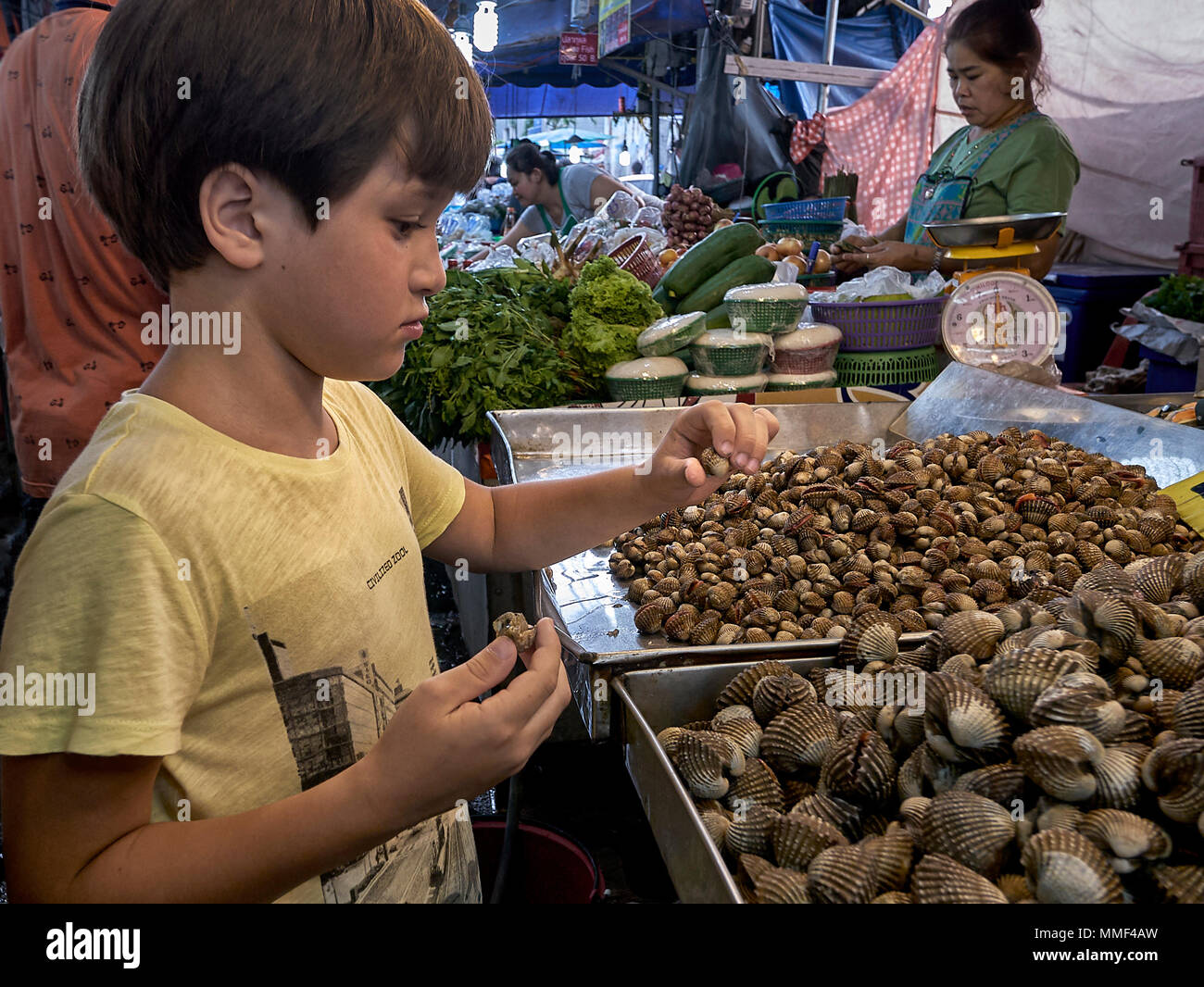 La curiosidad. Joven curiosamente estudiando los caracoles en un mercado callejero de Tailandia cale. Foto de stock