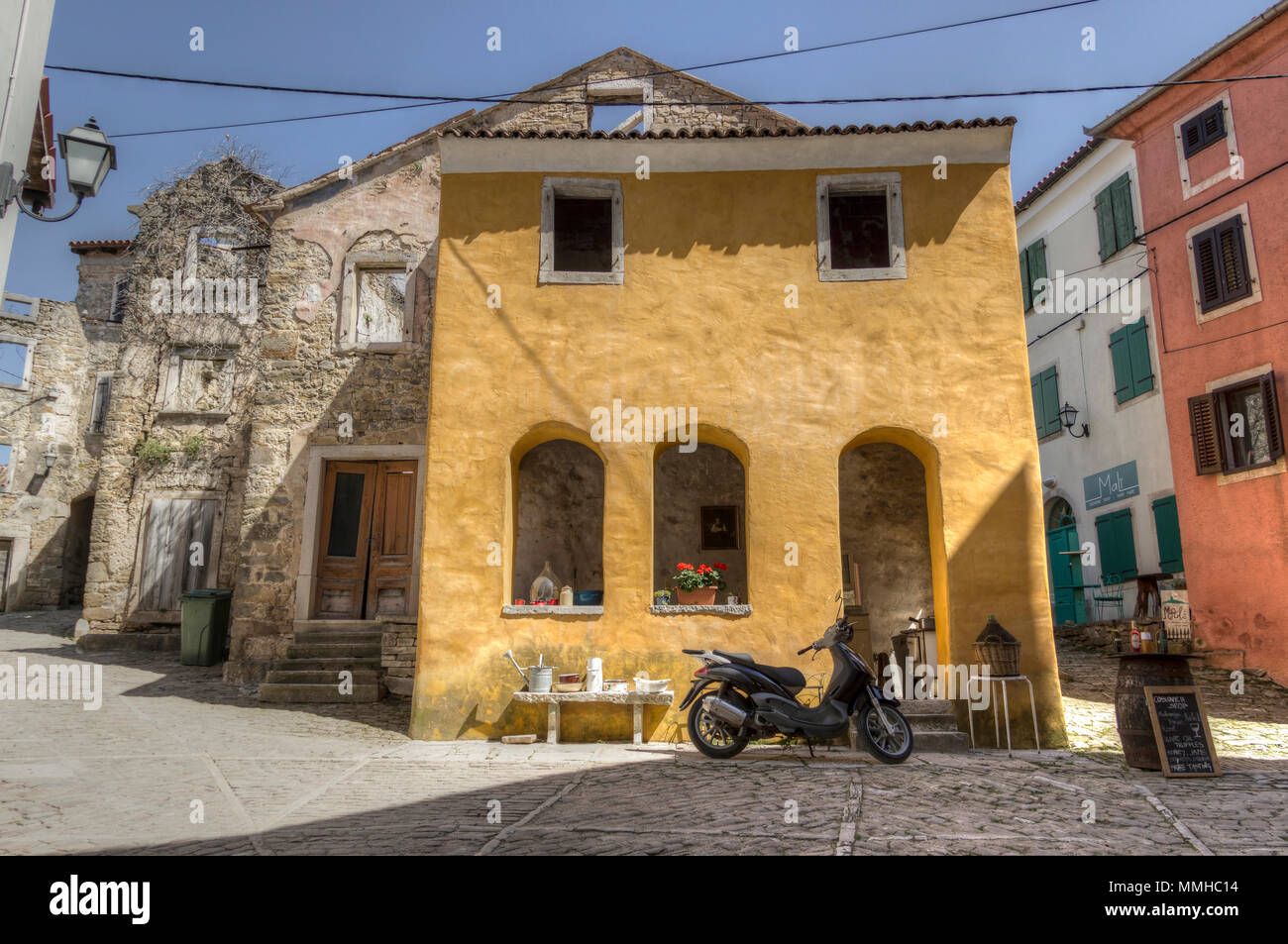 Central de Istria, Croacia, Abril 2018 - Scooter aparcado delante de una vieja casa amarilla en la esquina de dos calles de la antigua ciudad de Oprtalj Foto de stock