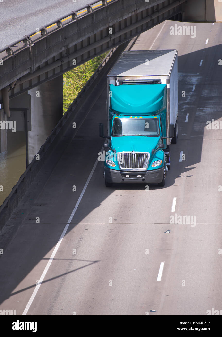 Big Rig verde semi larga distancia camiones frigoríficos con unidad sobre Camión semirremolque refrigerado conducción en carretera elevada sección junto al río bajo otro overpa Foto de stock