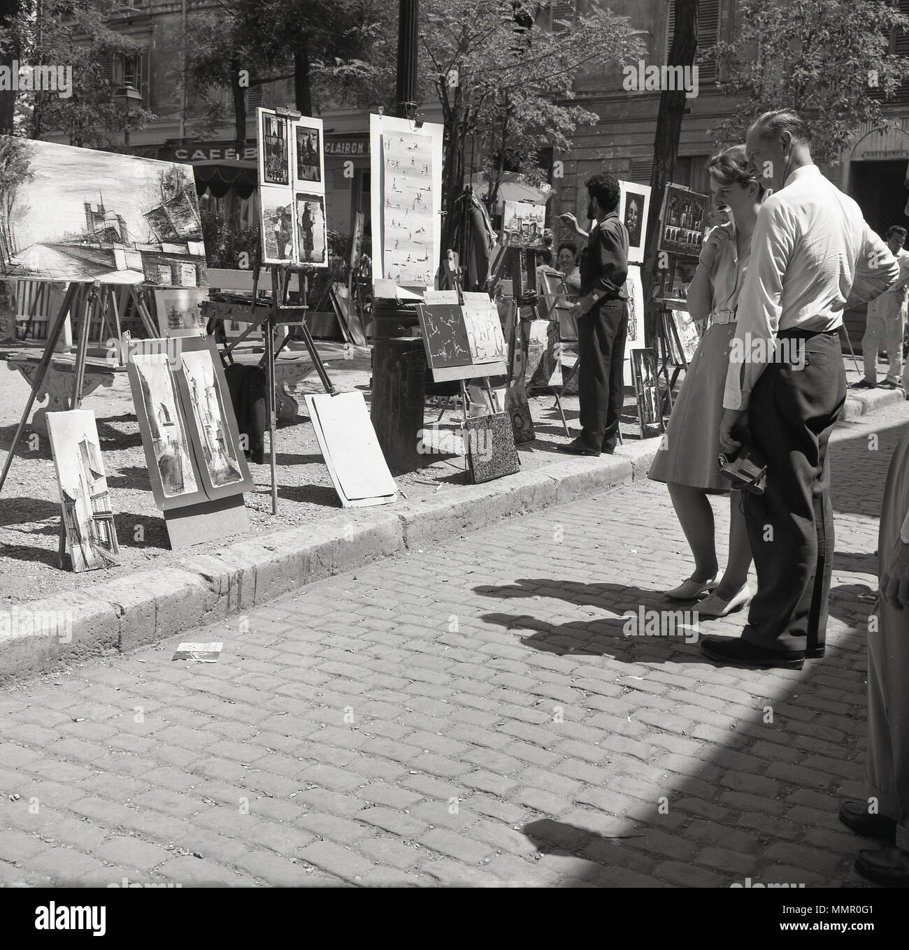 1950, par de pie mirando las obras expuestas en la plaza de Place du Tertre en Montmartre, París, Francia. El área, en la parte norte de la ciudad, es famosa por su historia artística y artistas de la calle utilice la plaza principal para crear y mostrar su trabajo. Foto de stock