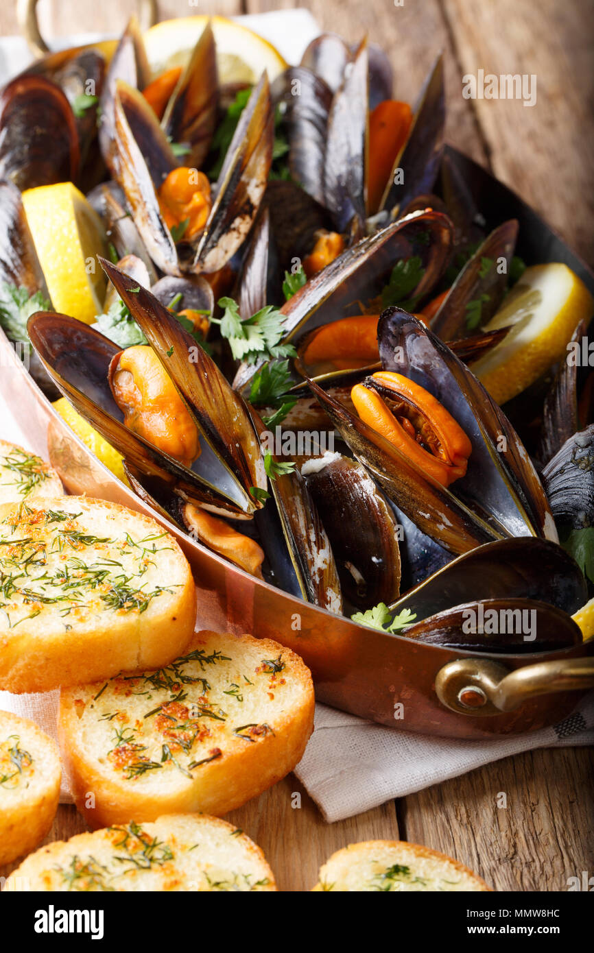 Francés de mariscos mejillones con limón, perejil y ajo de cerca en una olla de cobre y tostadas en la tabla vertical, estilo rústico. Foto de stock