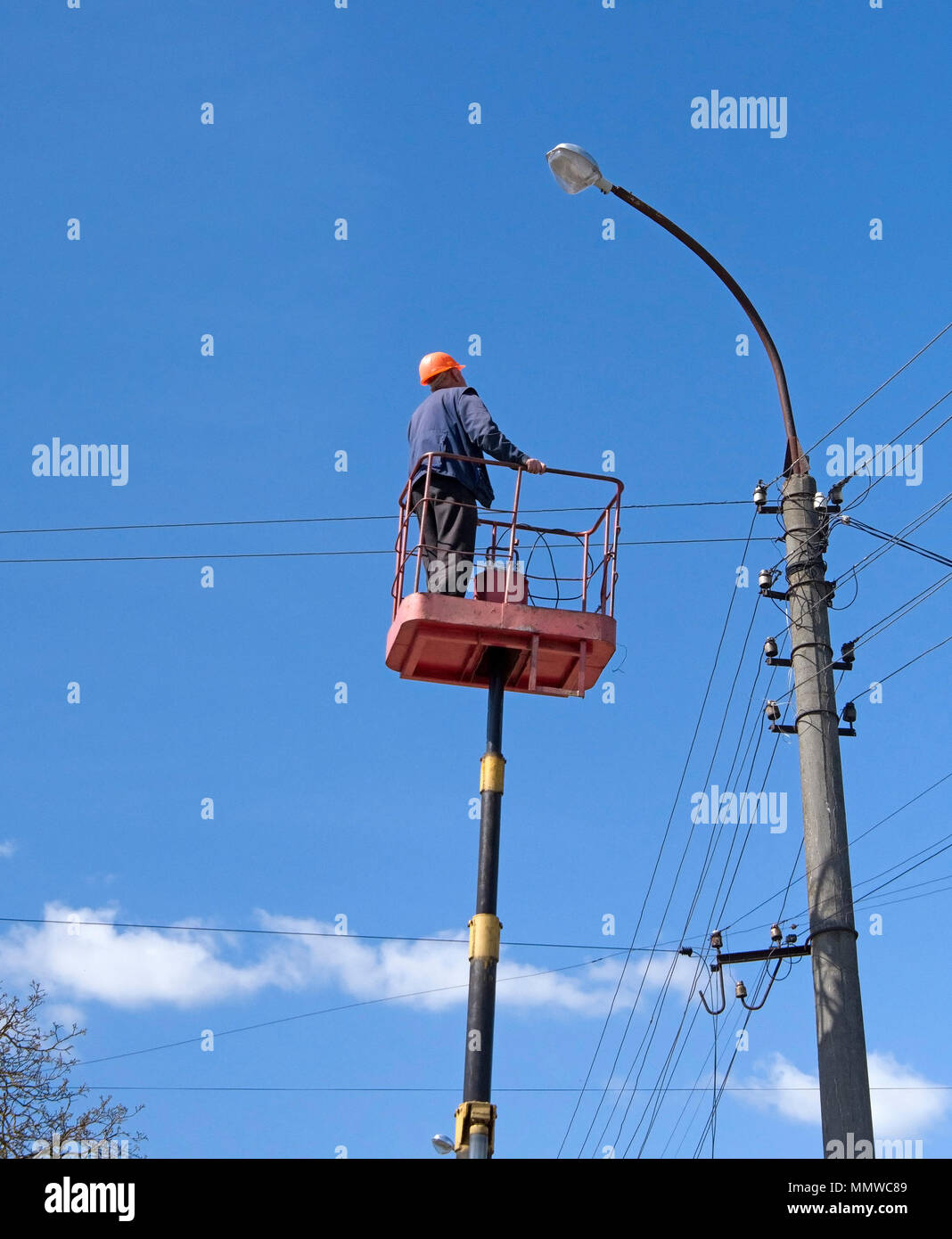 Electricista subir instalando nuevos trabajos sobre la energía eléctrica lámpara de la calle polo de hormigón en blue sky Foto de stock