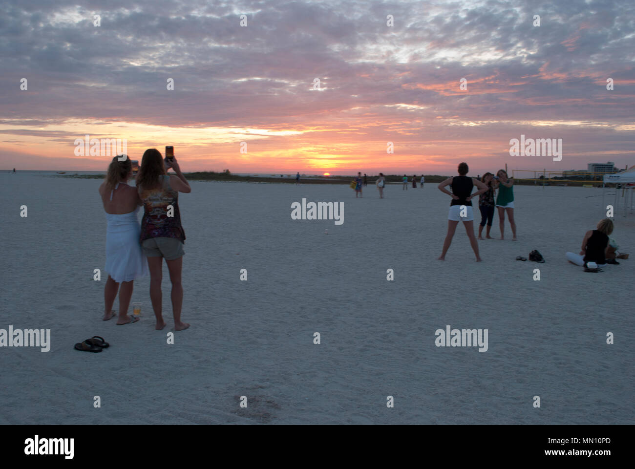 Mujer de grupo en la arena blanca de la playa viendo la puesta de sol. Las niñas fiesta en la playa. Feminidad moderna. Cielo dramático de sunrise Foto de stock