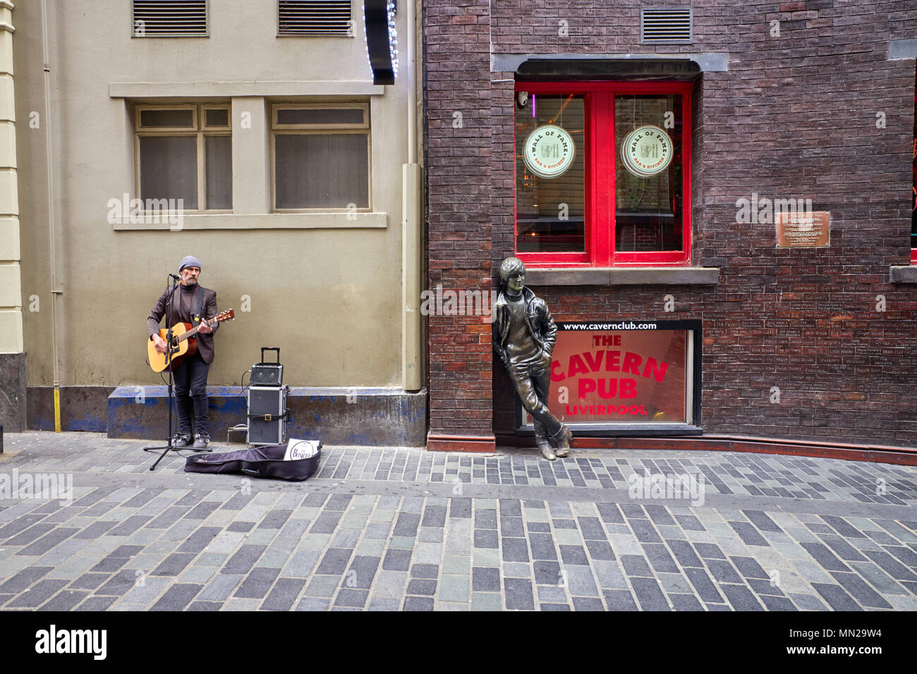 El músico callejero de Matthew Street, Liverpool, junto a la estatua de John Lennon y los ladrillos de la pared de la fama Foto de stock