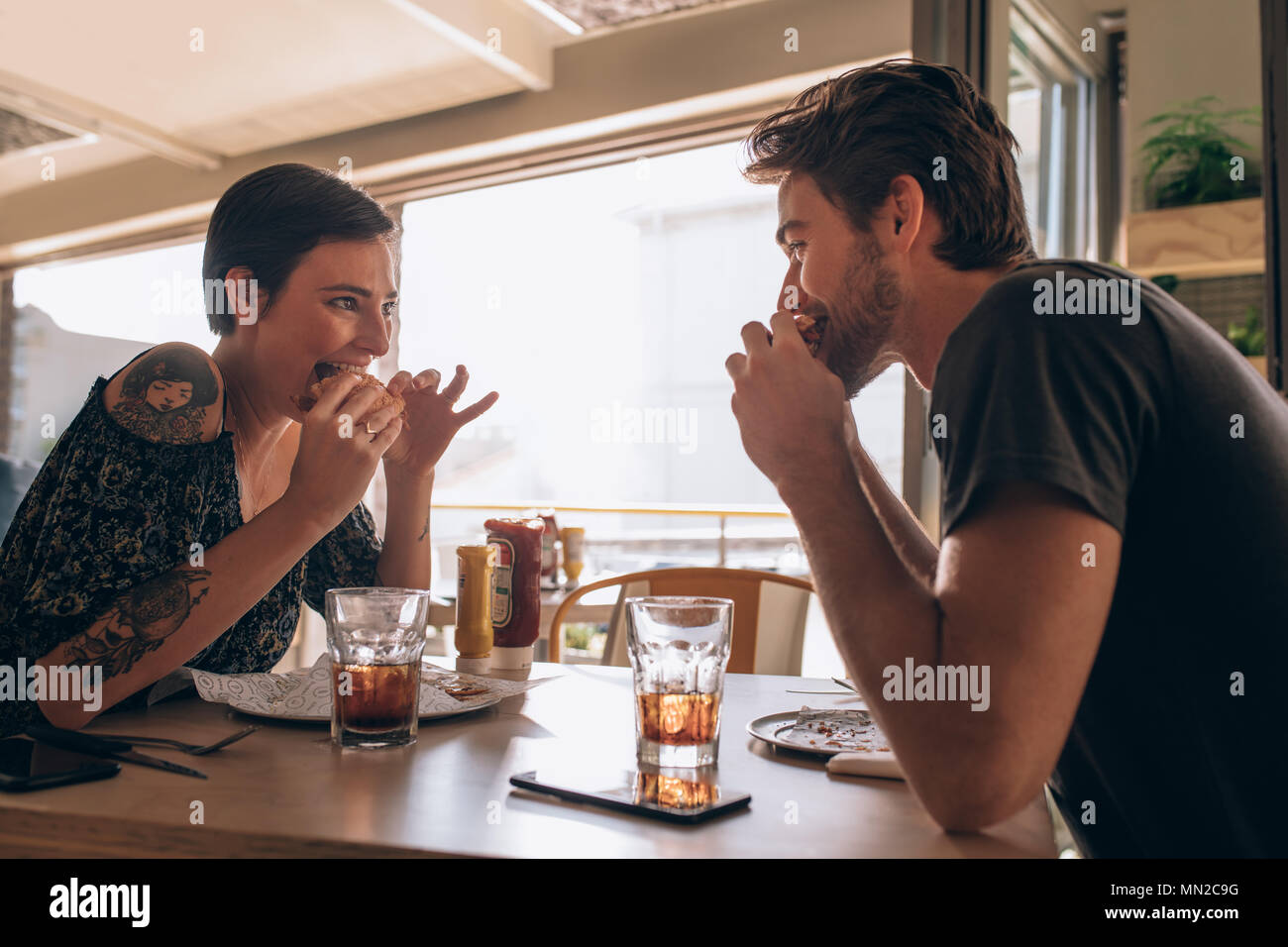Pareja joven disfrutar comiendo burger juntos. Mujer sonriente comiendo