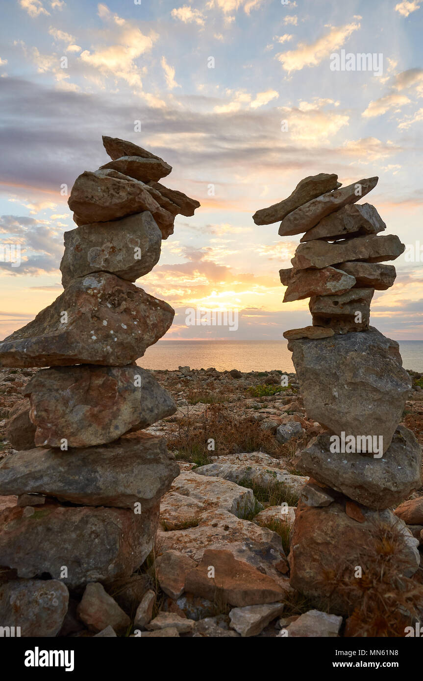 Montones de piedras apiladas al atardecer con el mar mediterráneo, rayos de sol y nubes en el cabo Cap de Barbaria en Formentera (Baleares, España) Foto de stock