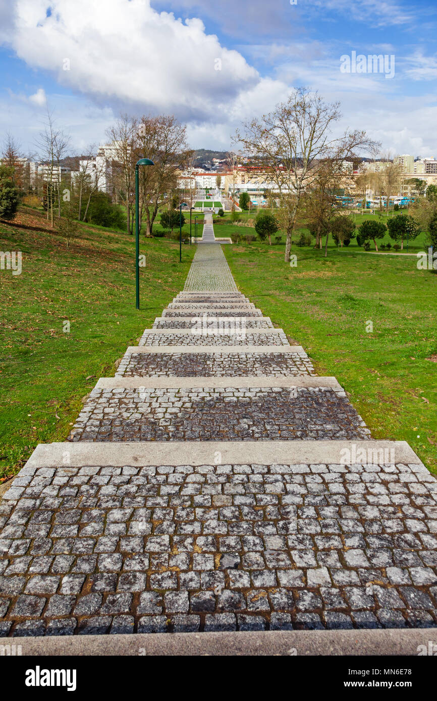 Escalera de adoquines vacía a través de los árboles y césped verde en Parque da Devesa Parque Urbano. Vila Nova de Famalicao, Portugal, en segundo plano. Foto de stock